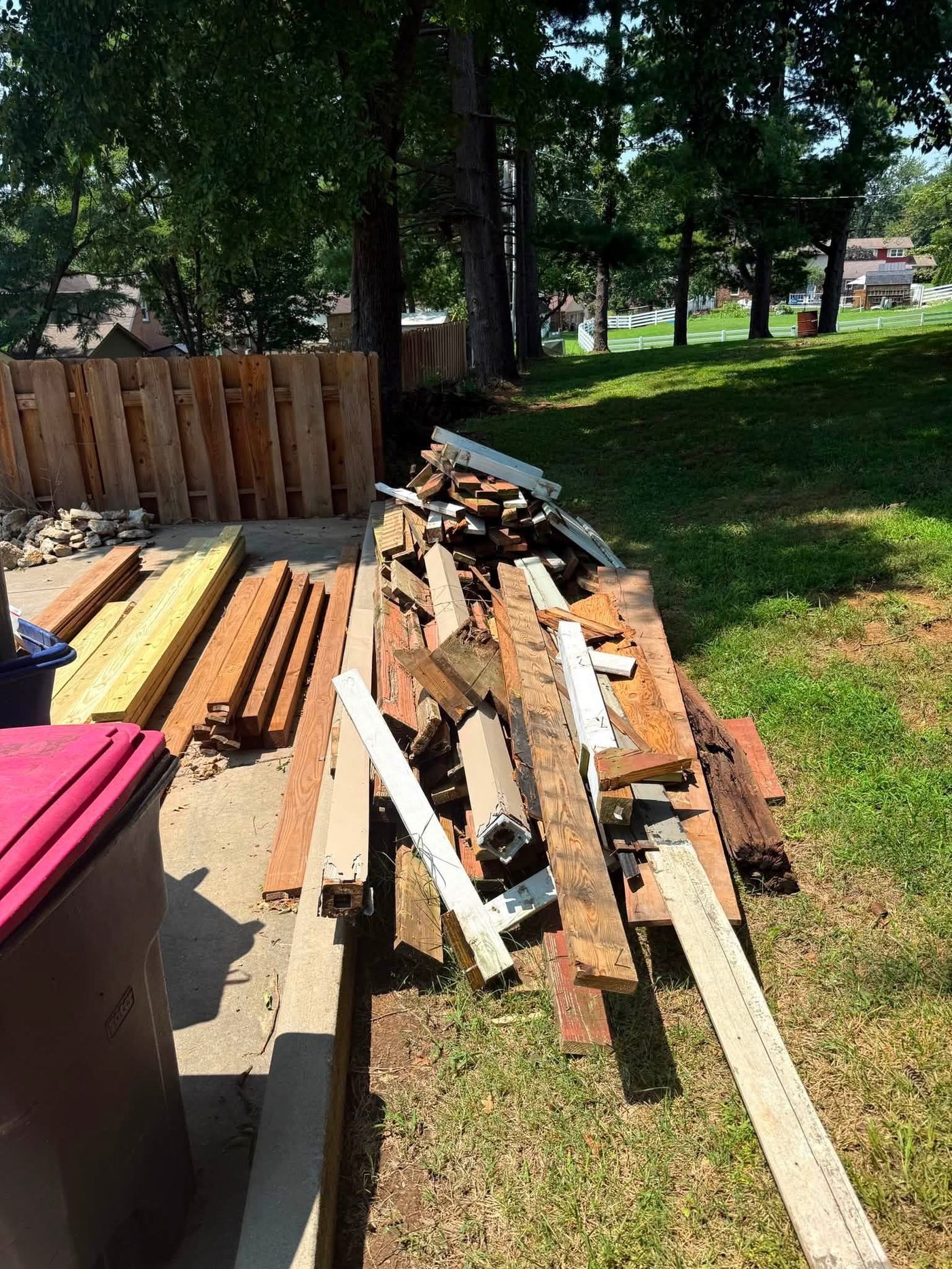Large pile of scrap wood and yard debris along a fence before removal